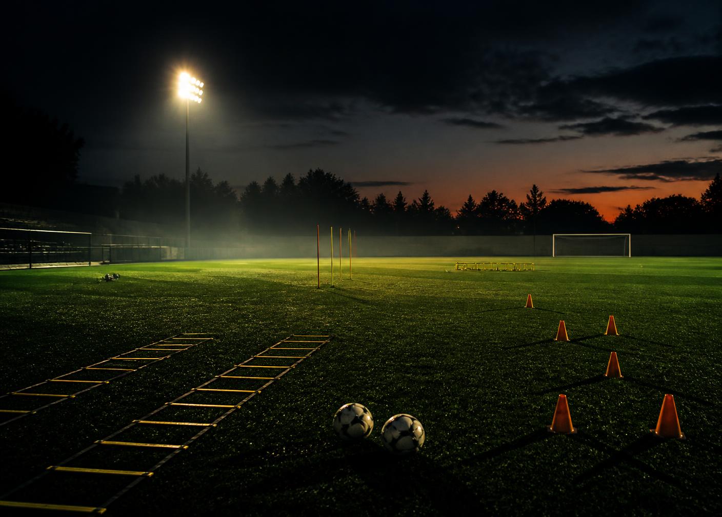 Floodlit training ground with cones, ladders and balls